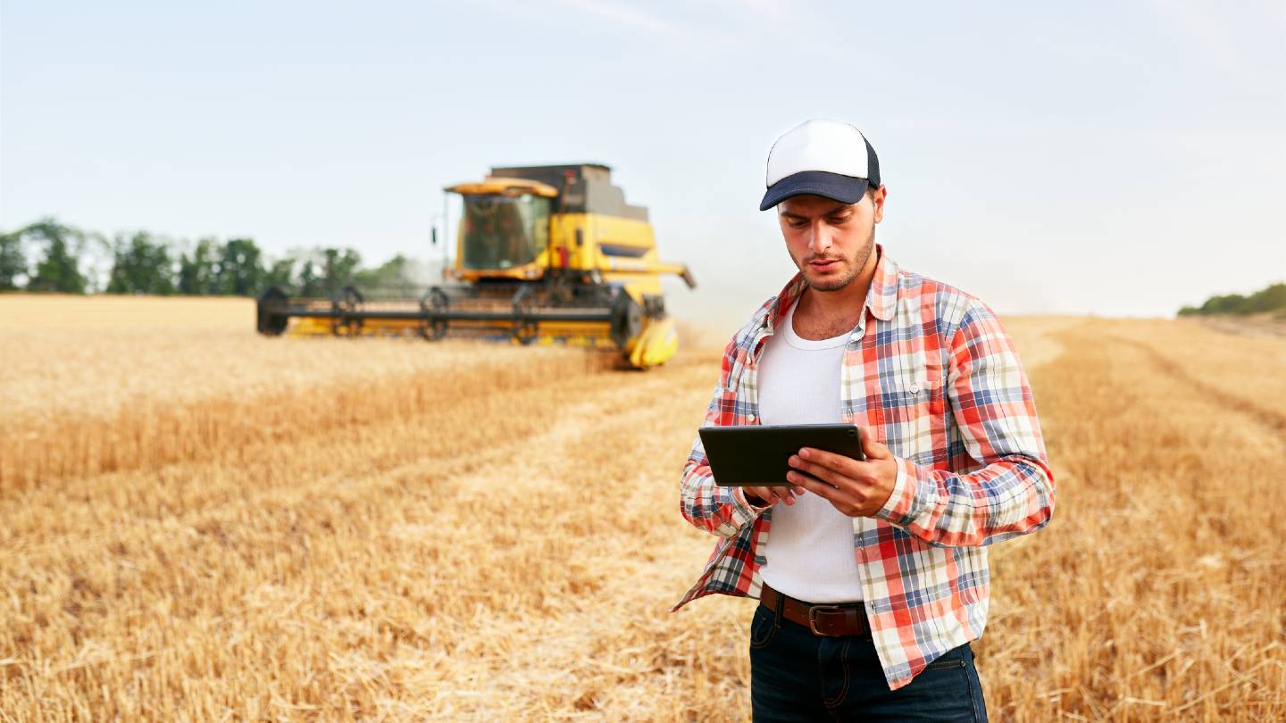 Farmer holding tablet for combine harvester guidance and control with modern automation system.
