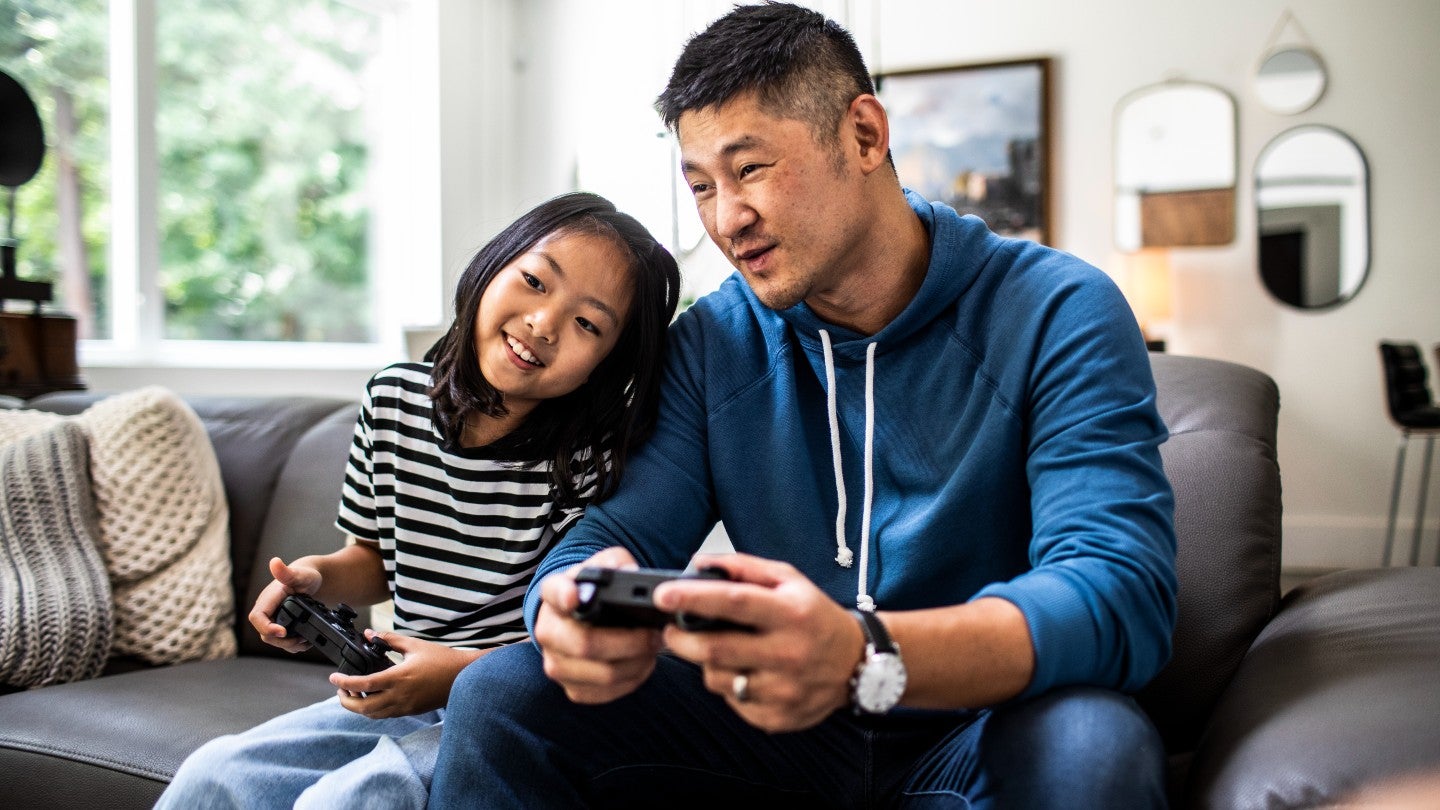 Adult with child holding console controllers and playing video games.