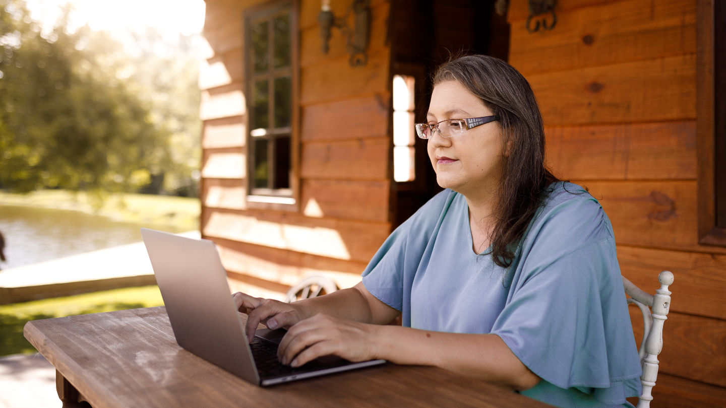 Woman using laptop on porch in rural area.